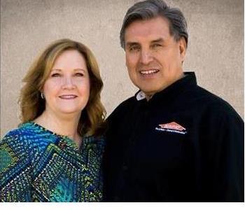 Male and female owners smiling in front of a cream background.